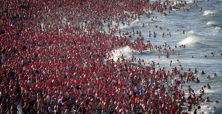 An aerial view taken on January 1, 2016 shows people with colourful bonnets taking part in the traditional New Year's dive ('Nieuwjaarsduik') on the beach of Scheveningen, The Netherlands. Tens of thousands of participants dip into the cold North Sea water every year in the Netherland's largest dive held at the beach of Scheveningen. It is a Dutch tradition that started in the 1960s, after a swim club decided to start the year with a plunge in the sea. All participants who take part in the dive receive a Unox cap named after the soup brand who sponsors the event. / AFP / ANP / STRINGER / Netherlands OUT