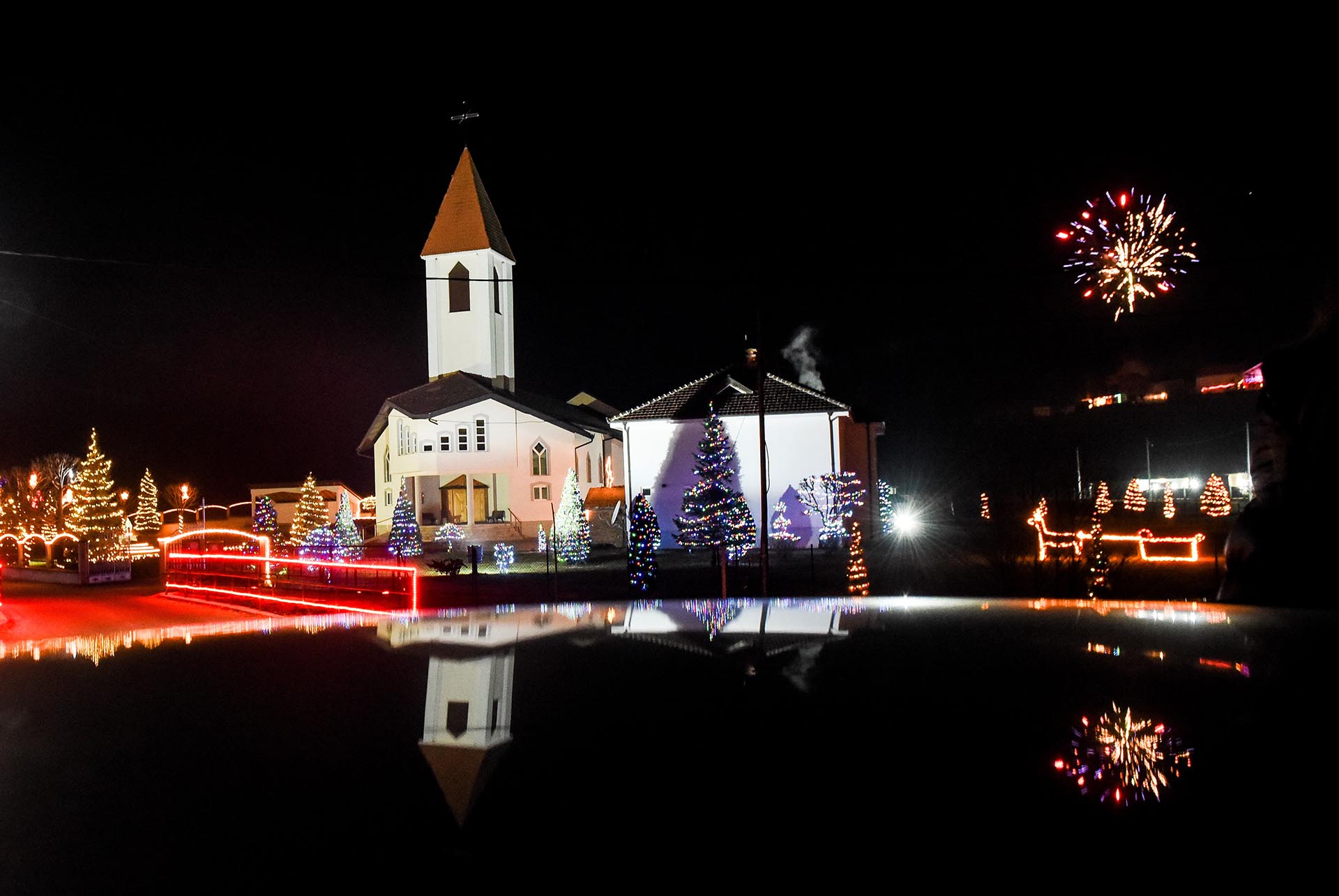 Fireworks explode above a Catholic Church decorated with lights on the eve of the Christmas mass in the village of Petrushan, 30 kms northwest of Prizren, on December 24, 2016. / AFP PHOTO / Armend NIMANI